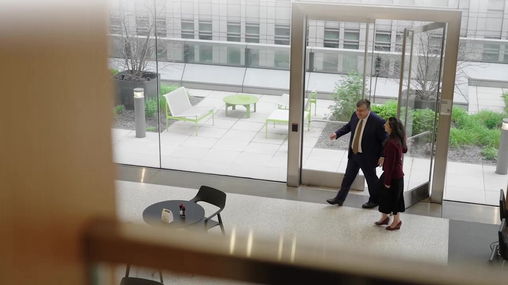 Hogan Lovells CEO Miguel Zaldivar walking through a bright, modern office lobby with a view of an outdoor patio area in the background